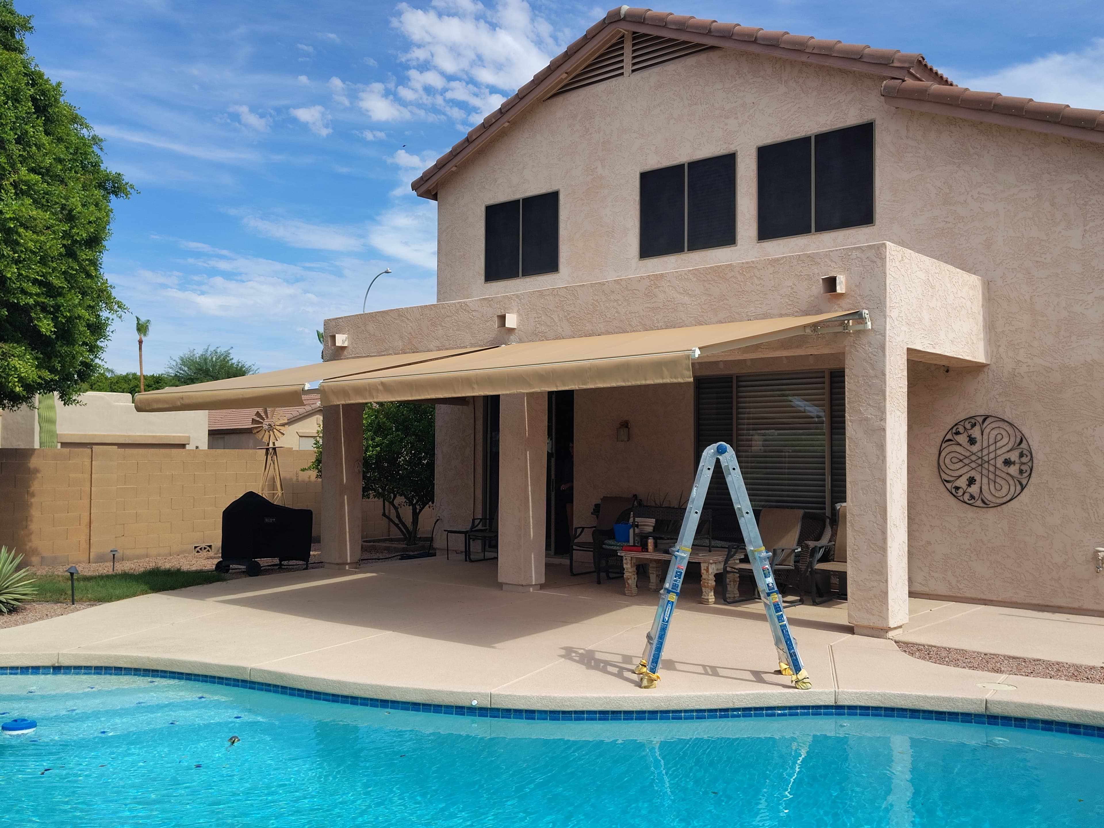Two restored tan retractable awnings shading a Chandler-area pool patio