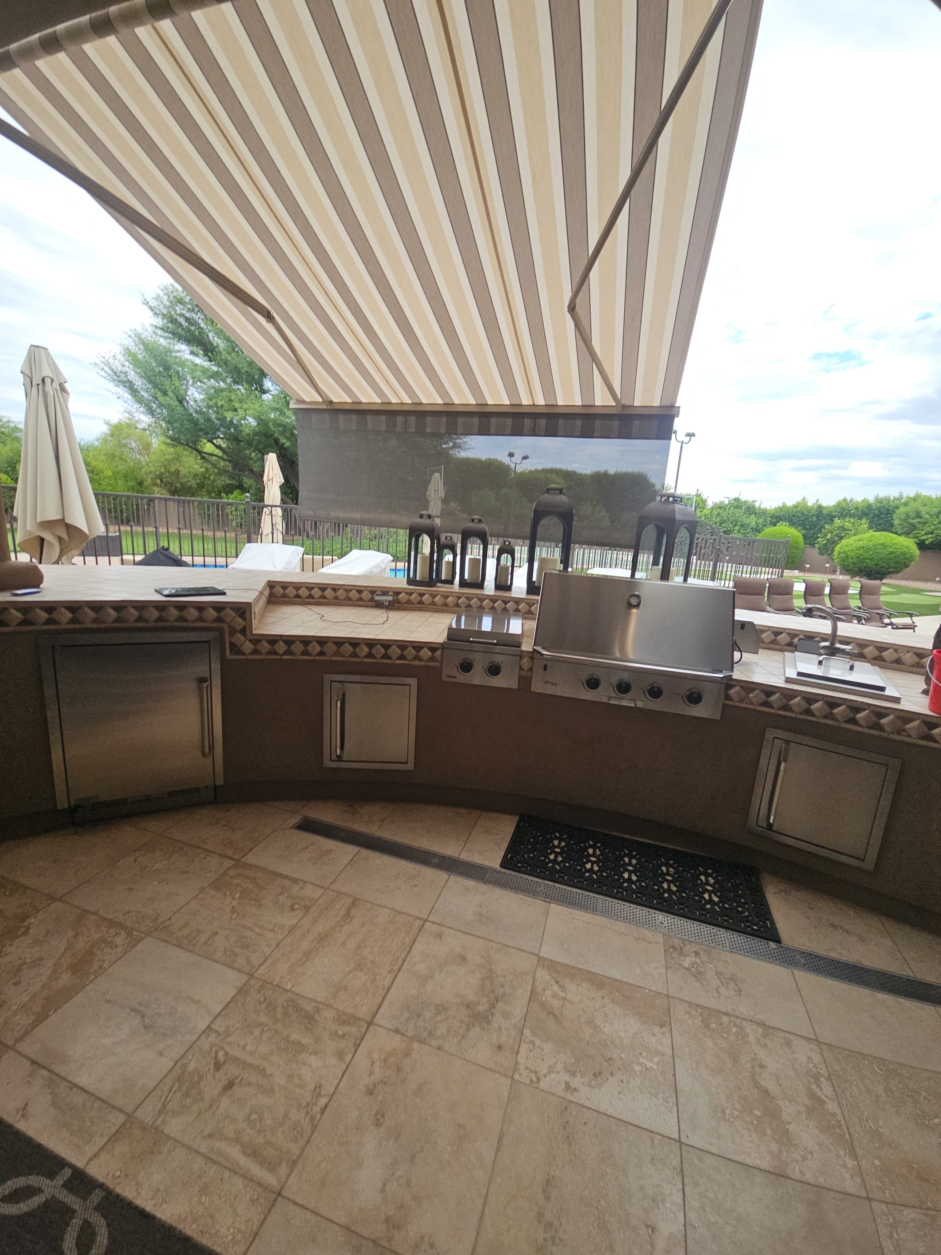 Striped retractable awning with integrated drop shade above an outdoor kitchen